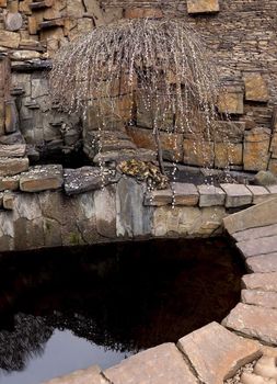 An artificial pond with a stone beach and a decorative plant in the spring