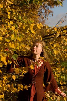 The blonde girl in medieval red dress in the autumn forest
