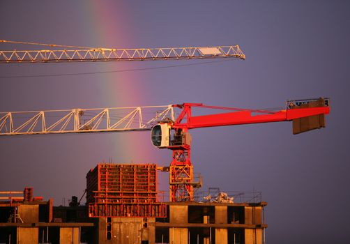 The elevating crane of construction on a background of the dark blue sky and a rainbow