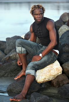 Portrait of the young African person sitting on stones at ocean. Bali. Indonesia
