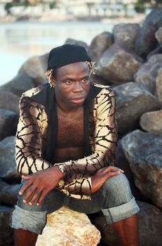 Portrait of the young African person sitting on stones at ocean. Bali. Indonesia