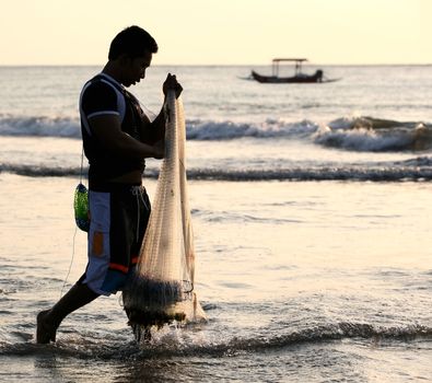 The person with a network fishing in a sunset. Indonesia. Bali