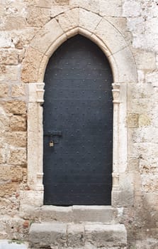 Old black wooden medieval door on limestone wall with antique sliding door bolt and padlock.