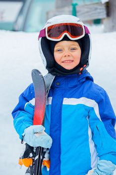 A photo of a Junior skier. Little cute boy with skis and a ski outfit. Vertical view