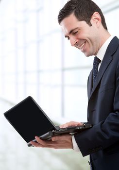 Handsome young business man in blue suit standing with laptop in office.
