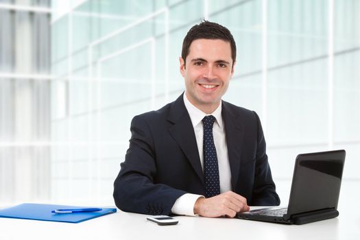 Handsome young business man in blue suit in office with laptop. 