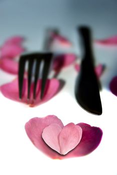 fork and knife with rose petals in a heart shape for concept on romantic dining