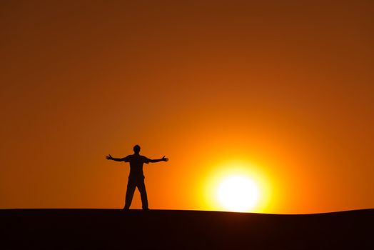 Man at orange sunset in desert with heroic achievement gesture