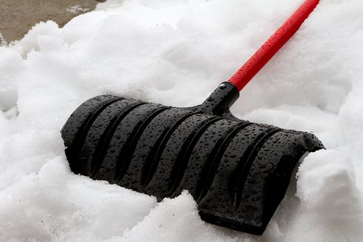 Snow shovel laying on the snow. small portion of clean sidwalk or driveway visable in the upper left corner