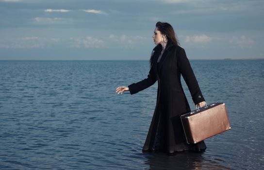 Woman in black coat going to the sea with luggage