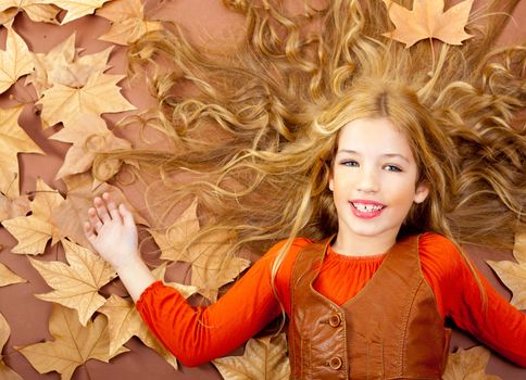 autumn fall little blond girl on dried tree leaves background and long spread hair