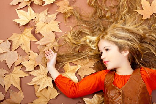 autumn fall little blond girl on dried tree leaves background and long spread hair