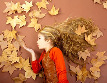 autumn fall little blond girl on dried tree leaves blowing wind with lips