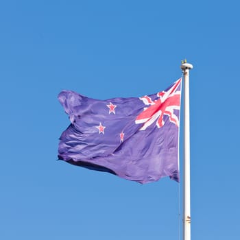 New Zealand national flag banner flying on pole in wind with blue sky background