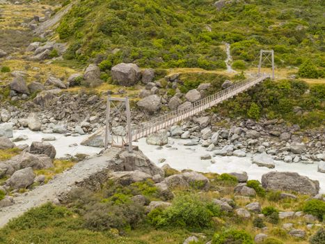Simple suspension swing bridge crossing a rocky mountain river in Aoraki/ Mount Cook National Park South Island New Zealand