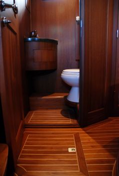 Impression of the interior of a small deluxe yacht, showing the intimate forward cabin and the heads compartment, displaying the v-shaped bunk beds, 360 degrees mahogany wood panelling, the shower and toilet compartment, including sink, and the custom built storage cabinets