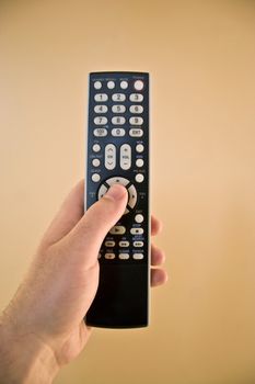 A hand holding a remote control isolated over a gold background.