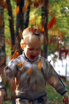 The child throws autumn leaves