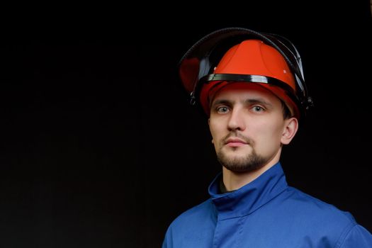 The worker in overalls and a helmet on a black background 