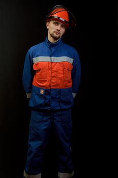 The worker in overalls and a helmet on a black background 