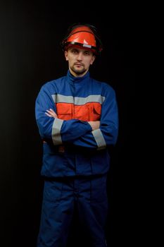 The worker in overalls and a helmet on a black background 