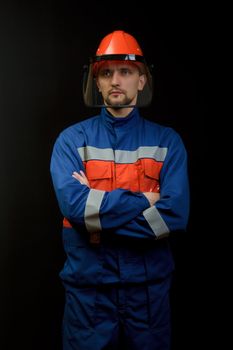 The worker in overalls and a helmet on a black background 