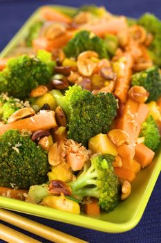 Vegetarian stir-fry Thai-style with broccoli, carrot, onion, mango with fried coconut flakes and peanuts (Selective Focus, Focus on the broccoli in the middle of the image)