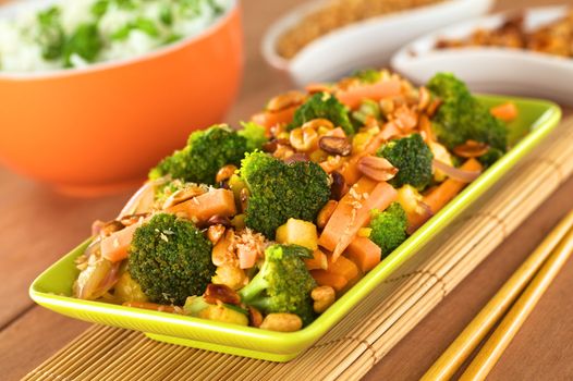 Vegetarian stir-fry Thai-style with broccoli, carrot, onion, mango with fried coconut flakes and peanuts (Selective Focus, Focus on the broccoli in the middle of the image)