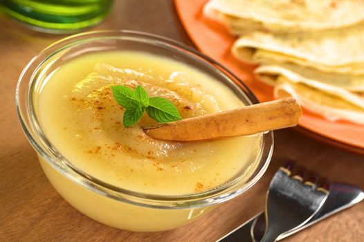 Fresh home-made apple sauce with cinnamon garnished with mint and crepes in the back (Selective Focus, Focus on the front of the mint leaf) 