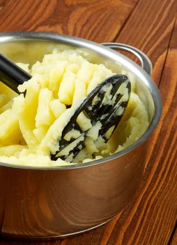 Preparing Mashed Potato in Stainless Steel Pan with Black Potato Masher on Wooden background