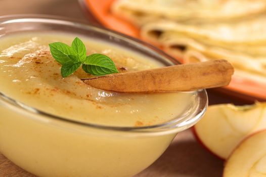 Fresh home-made apple sauce with cinnamon garnished with mint and crepes in the back (Selective Focus, Focus on the front of the mint leaf) 