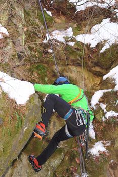 man in green jacket climbing a dry face of rock in winter