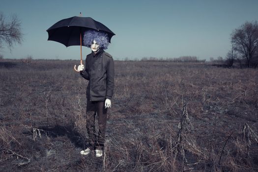 Sad clown outdoors hodling black umbrella