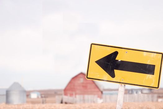 Street sign in rural area with muted red barn and farm buildings in the background