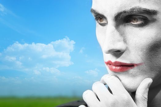 Pensive clown outdoors with theatrical makeup. Horizontal photo, artistic vibrant colors added