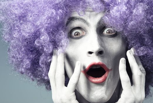 Clown with artistic makeup and wig expressing surprise. Natural light and colors