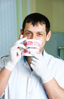 cheerful young dentist teaching a patient to brush teeth and having fun