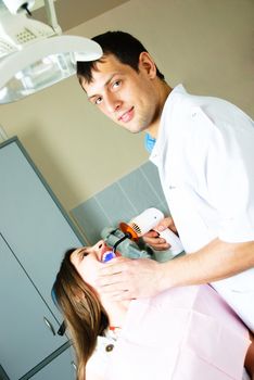 young dentist curing the patient's teeth with ultraviolet in his office