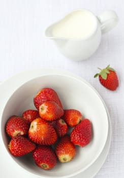 A bowl of ripe strawberries with a jug of cream in the background