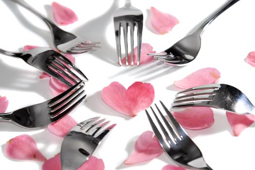 forks surrounding a heart shape petal with rose petals for a concept on romantic dining on white background