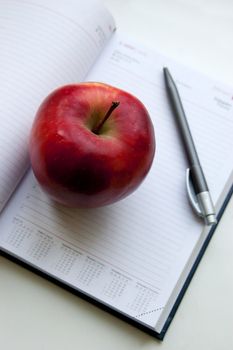 An apple lay on notebook next to pencil