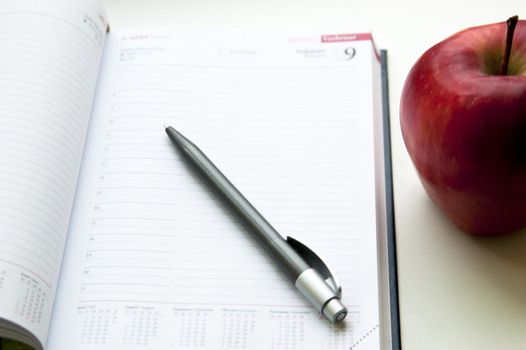 An apple lay near notebook next to pencil