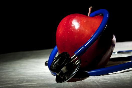 An red apple surrounded by blue medical stethoscope