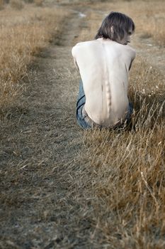 Single topless man outdoors sitting at the country road. Rear-vew photo. Artistic colors added