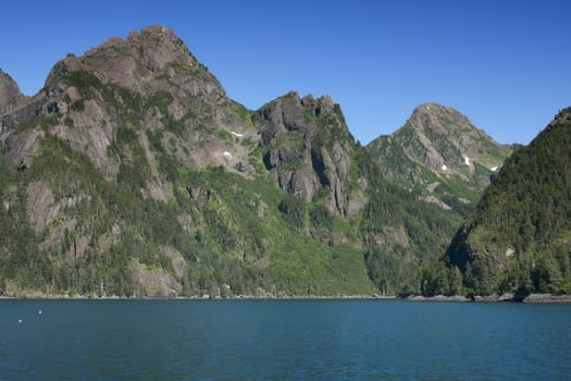 Summer time creates green patches of vegetation against brown rocky mountains with white snow remnants.