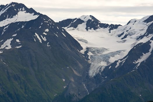 Thick flow of snow and ice cuts valley in dark mountain with green flanks.