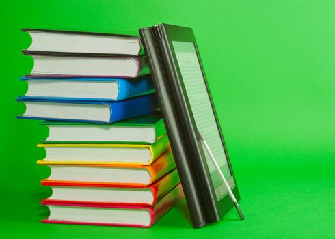Electronic book reader with stack of printed books over green background