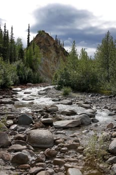 Portrait image with river flowing towards the viewer. Rocky hill, forested sides.