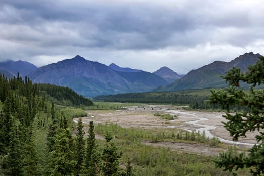 Spectacular wide view over valley with narrow meandering river and mountains in the background.