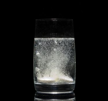 aspirin tablet in glass of water over black